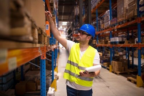 Profissional utilizando colete de segurança enquanto organiza produtos em estoque de armazém.