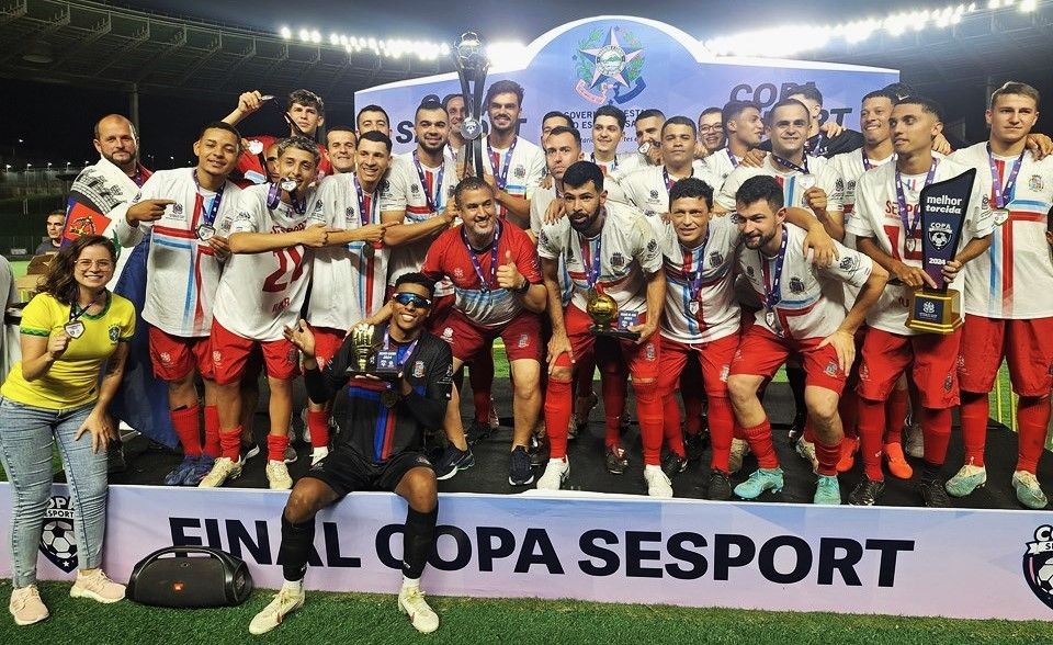Jogadores da Seleção de Iúna comemoram o título da Copa Sesport no Estádio Kleber Andrade, exibindo troféu e medalhas após a conquista estadual.