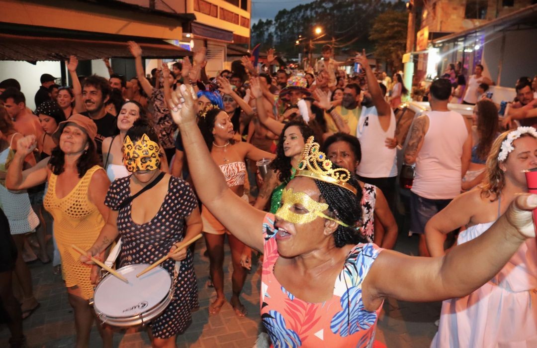 Foliões fantasiados cantam e dançam no meio da rua durante o Carnaval 2026 em Patrimônio da Penha, com destaque para mulher usando máscara dourada e coroas, em clima de festa coletiva.