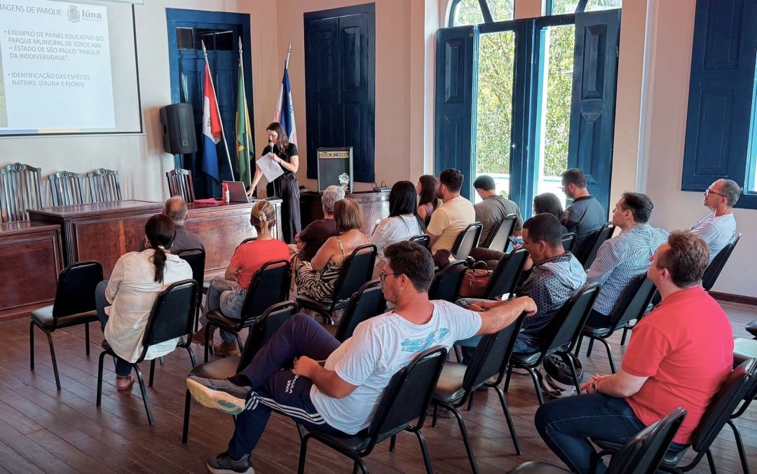 Participantes acompanham apresentação técnica durante Audiência Pública sobre a recategorização da Reserva Jovelino Nunes, em Iúna, com projeção de imagens e mapas da área ambiental.