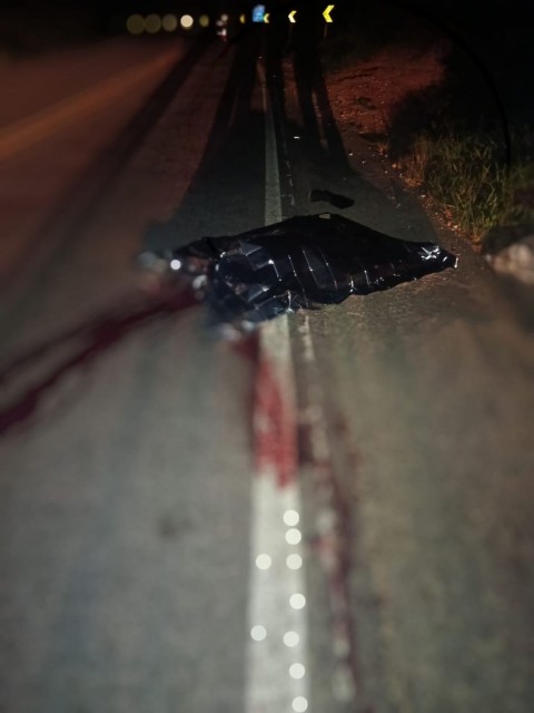 Trecho da BR-482 à noite com corpo coberto por lona após acidente com ciclista na zona rural de Guaçuí.