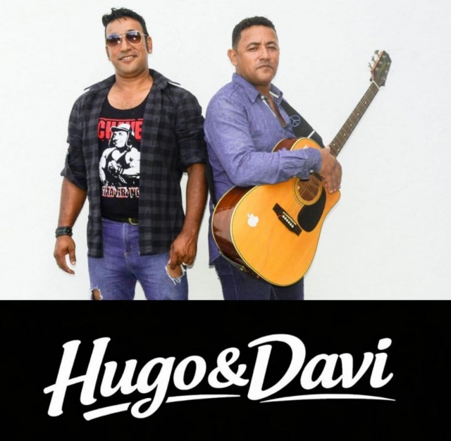 Imagem promocional da dupla Hugo & Davi. Os dois artistas estão em pé, um deles segurando um violão, diante de fundo neutro. Abaixo, aparece o nome da dupla em destaque com a identidade visual oficial.