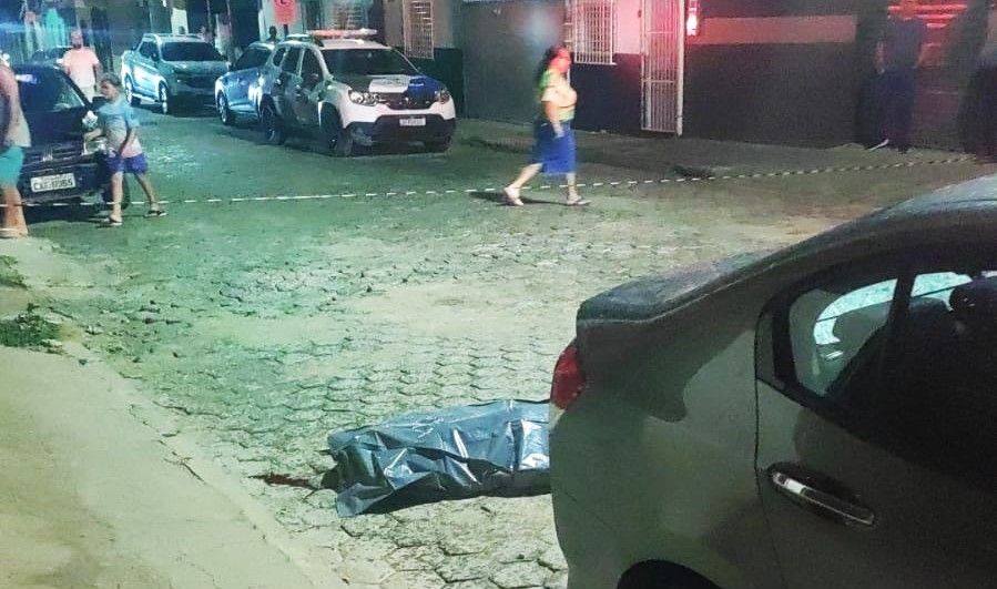 Corpo está coberto por plástico na via pública, enquanto moradores acompanham a ocorrência de homicídio ocorrido no bairro Boa Esperança, em Ibatiba.