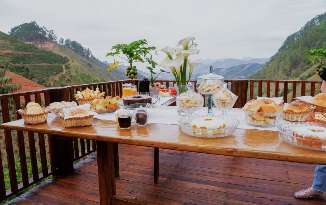Mesa com café colonial e produtos artesanais em varanda com vista para as montanhas do Caparaó em propriedade da Rota Cafés de Muniz Freire.