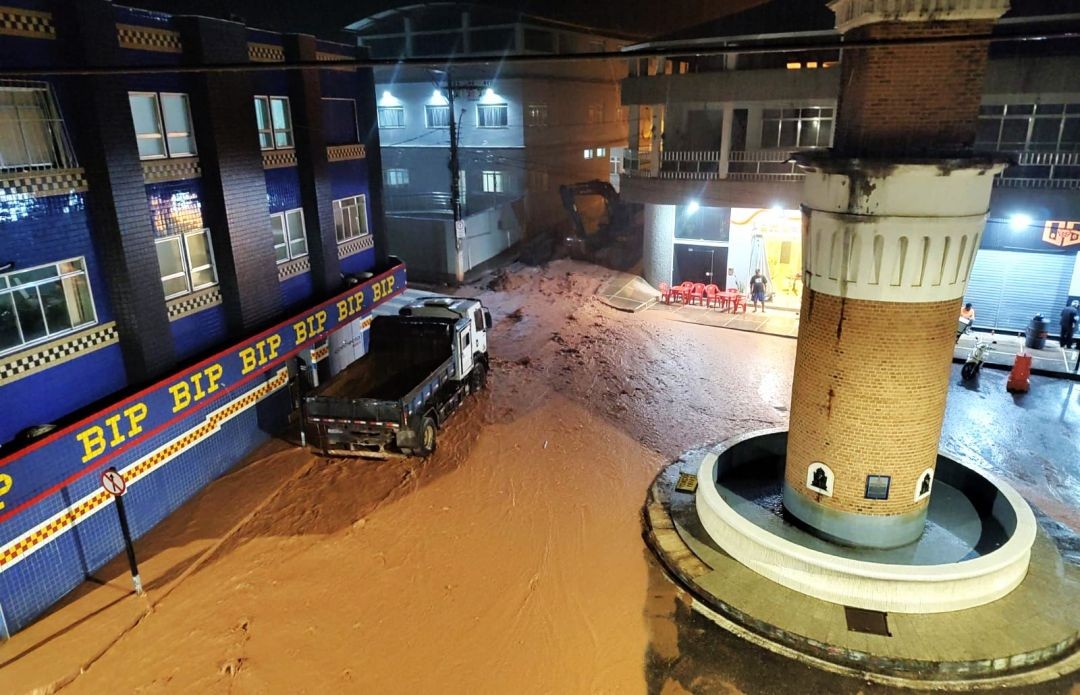 Foto noturna da Praça Antônio Guizzardi com água cobrindo parte da via, durante a forte chuva desta quarta-feira (11)