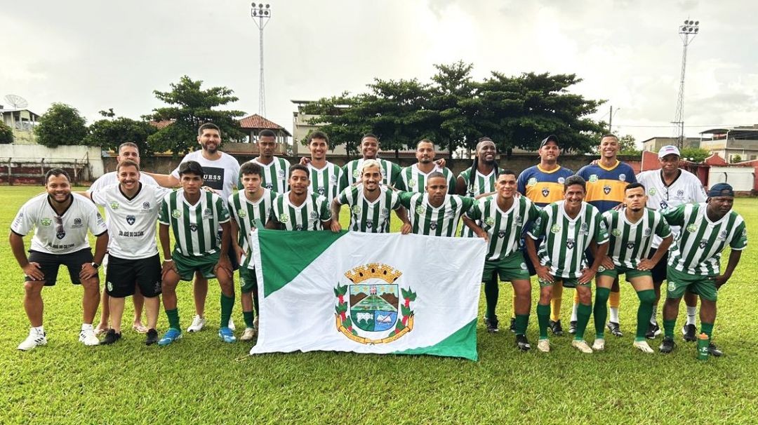 Jogadores da equipe de futebol masculino de São José do Calçado posam para foto oficial no gramado, segurando a bandeira do município à frente do time.