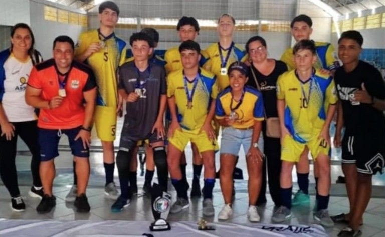 Integrantes da equipe Assopais (São Gabriel da Palha) comemorando com medalhas no peito e troféu à frente no Ginásio de Iúna.