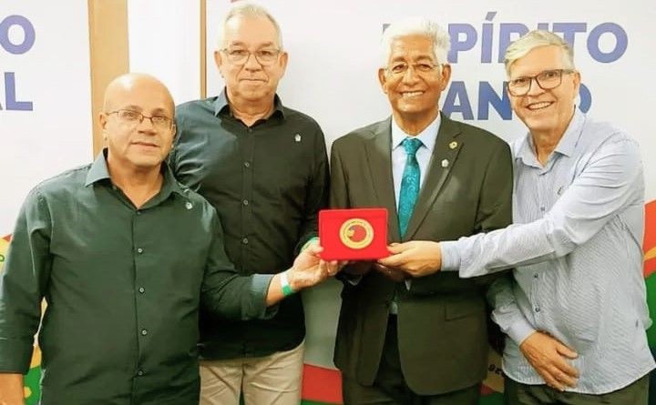 Quatro homens posam sorrindo em frente a um painel escrito 