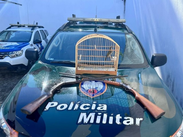 Viatura da Polícia Militar com armas apreendidas e gaiola contendo ave silvestre em cima do capô