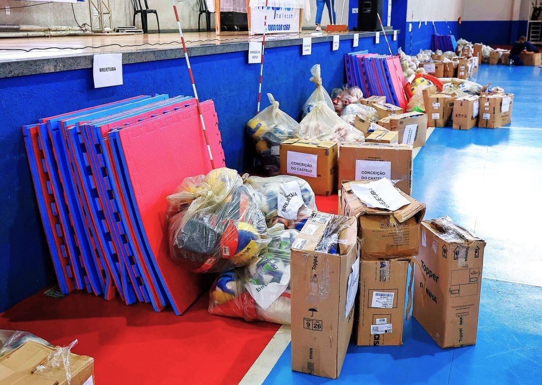Materiais esportivos organizados em quadra de ginásio durante entrega do projeto Campeões de Futuro em Iúna, com kits destinados a diferentes modalidades esportivas.