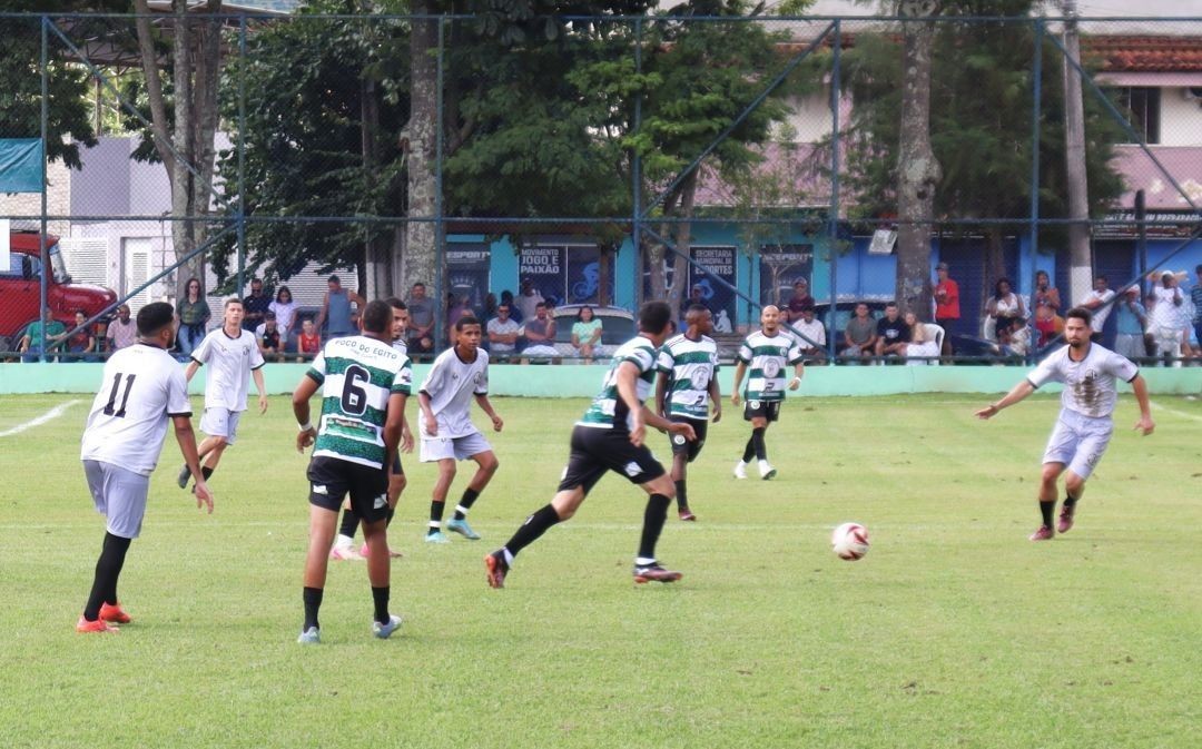 Partida de futebol amador em estádio municipal, com jogadores em campo durante competição regional em Dores do Rio Preto.