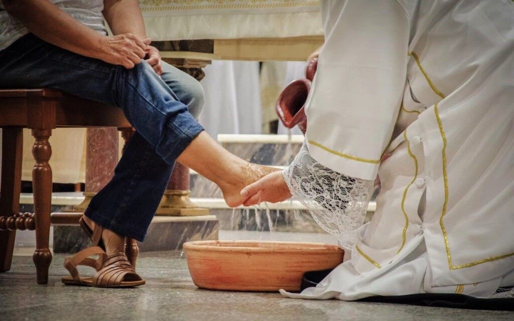 Fiéis participam do rito do lava-pés durante celebração da Quinta-feira Santa, em ambiente religioso, simbolizando gesto de serviço e humildade.