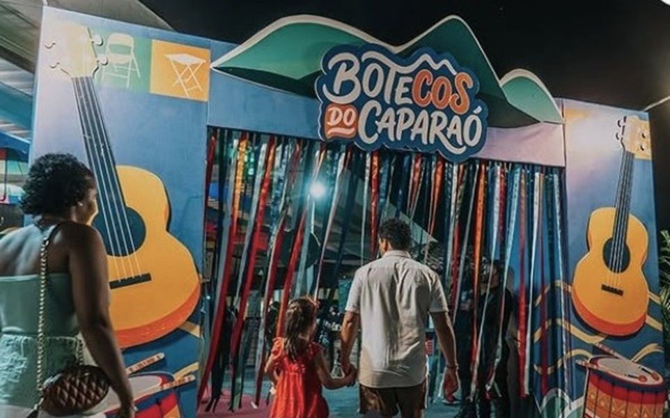 Imagem da entrada decorada do Festival Botecos do Caparaó, com elementos musicais e uma mulher, uma criança e um homem se dirigem para essa entrada.