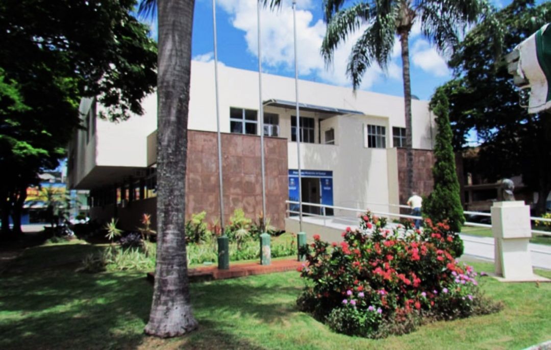 Fachada da Prefeitura de Guaçuí, com prédio administrativo cercado por jardim, árvores e mastro de bandeiras na área central da cidade.
