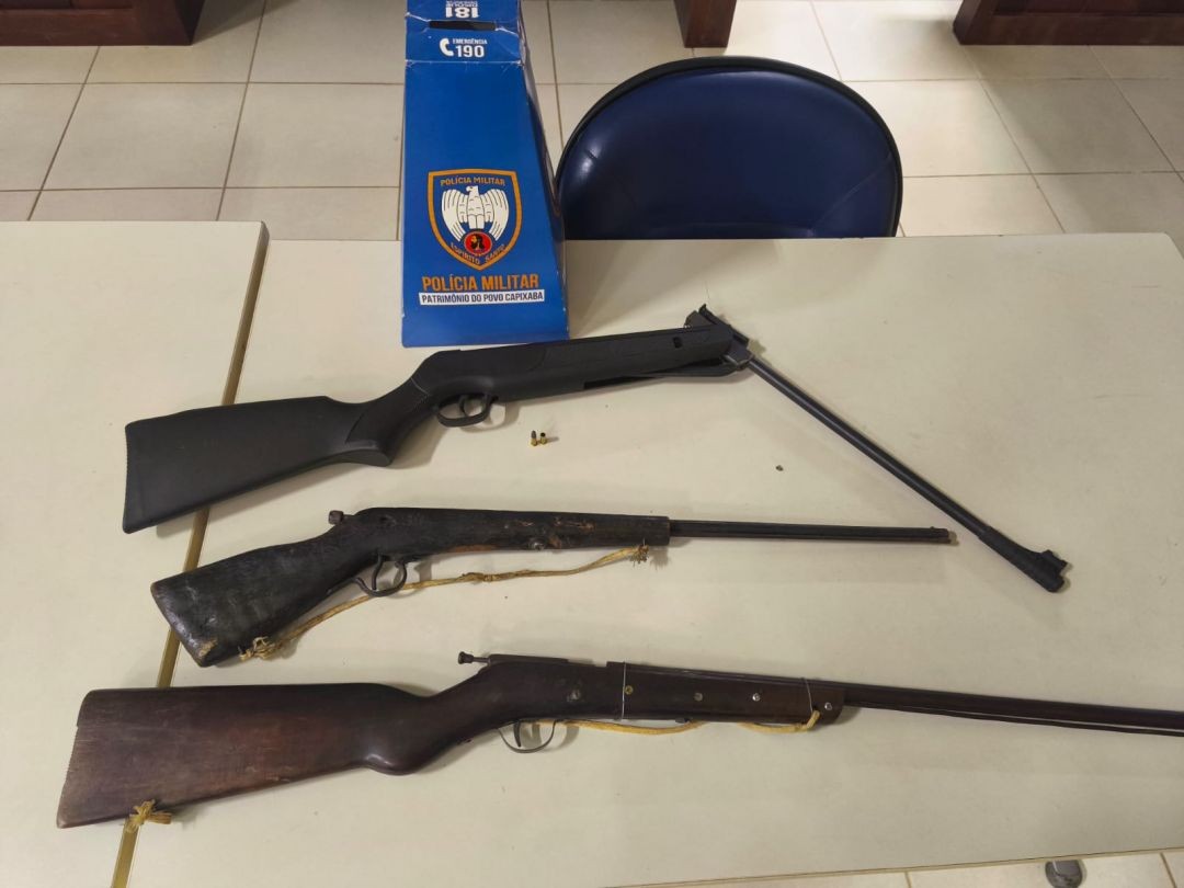 Imagem mostra três armas longas apreendidas pela Polícia Militar, incluindo duas espingardas artesanais e uma de chumbinho, sobre uma mesa em ambiente interno.