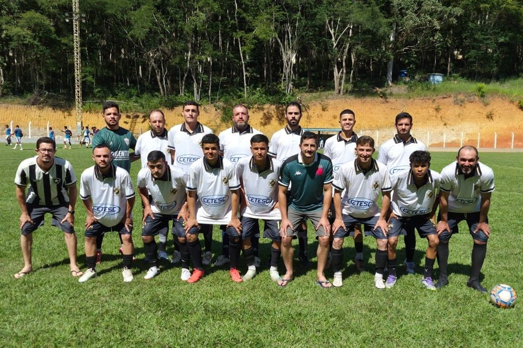 A imagem apresenta a equipe do Atlético União posando como campeã do Torneio do Trabalhador. O time, composto por dezessete homens adultos está organizado em duas fileiras (em pé e agachados) sobre a grama sob luz solar intensa. A maioria dos jogadores veste o uniforme oficial: camisa branca com gola polo preta, detalhes pretos nos ombros e a inscrição 