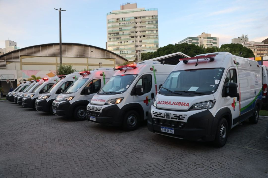 Fileira de ambulâncias brancas da marca Fiat, modelo Ducato, estacionadas em um pátio de blocos sextavados. Os veículos possuem a inscrição 
