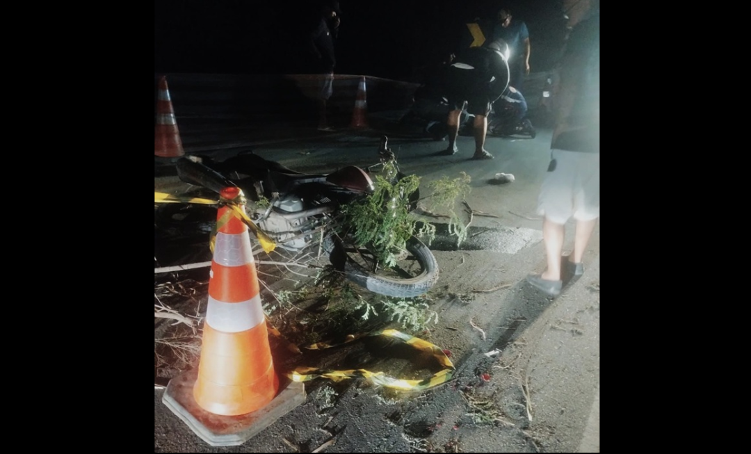Motocicleta caída na pista durante atendimento de ocorrência de acidente na zona rural de Alegre, à noite, com cones de sinalização e equipes atuando no local.