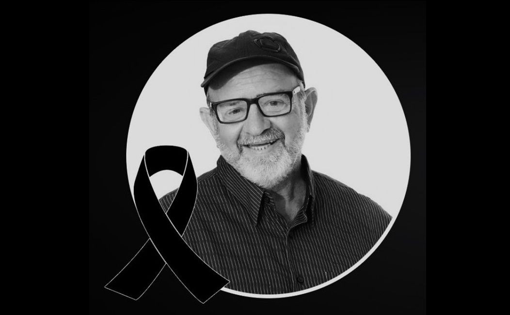 Imagem em preto e branco mostra Cláudio Deps de Almeida sorrindo, usando boné e óculos. Ao lado da foto, há um laço preto em sinal de luto.