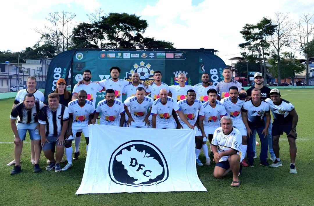 Foto oficial da equipe do Douradense (DFC). Jogadores e comissão técnica posam no centro do campo vestindo uniformes brancos com detalhes coloridos e pretos. À frente do grupo, dois homens seguram uma bandeira branca com o mapa do Brasil e as letras 