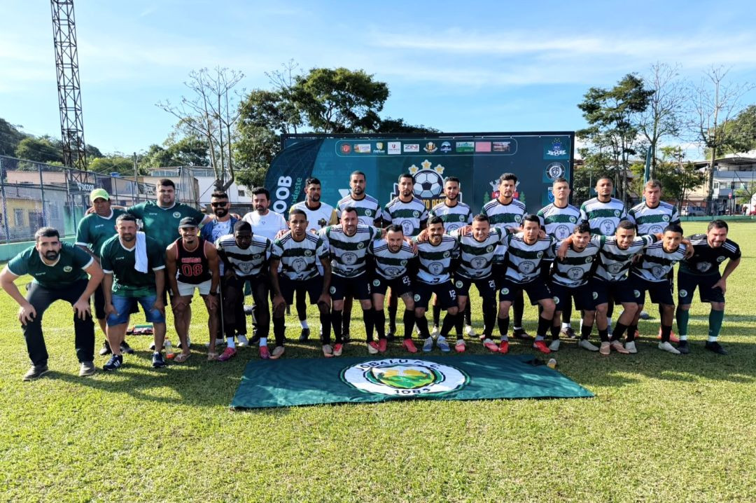 Foto oficial da equipe do Jobalu F.C. posicionada no gramado. Os jogadores vestem uniforme com listras horizontais verdes, brancas e pretas, calções pretos e meiões pretos. Comissão técnica veste camisas verdes. À frente do grupo, uma bandeira verde e branca do Jobalu F.C. com o ano 1982 está estendida no chão. Ao fundo, um painel do Campeonato Regional e banners do Sicoob.
