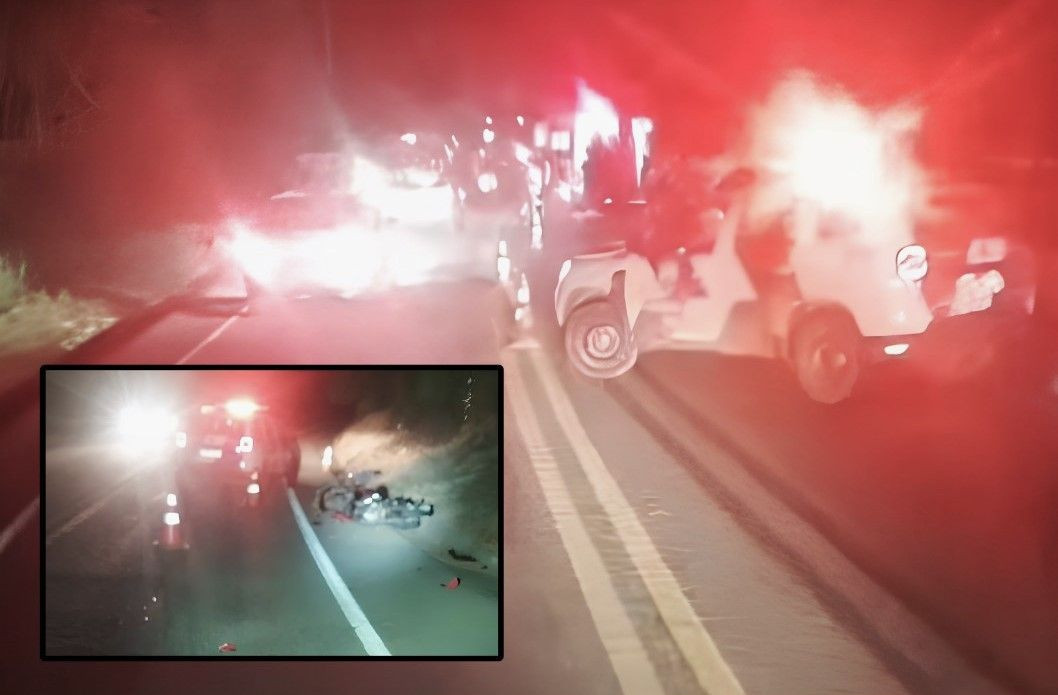 Fotografia noturna em uma rodovia asfaltada com forte iluminação vermelha proveniente de giroflex de viatura policial, criando um efeito de névoa luminosa. À direita, um veículo utilitário branco está estacionado na margem da pista com marcas de pneus visíveis no asfalto. No canto inferior esquerdo, há um detalhe ampliado em destaque retangular mostrando um trecho da pista sinalizado com cones de trânsito e uma motocicleta caída de lado próxima ao acostamento, sob a luz dos faróis de uma viatura.