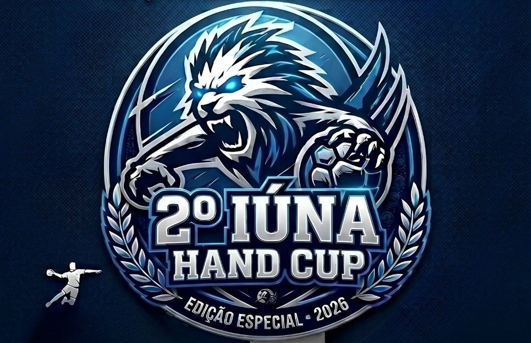 Logotipo circular do torneio 2º Iúna Hand Cup Edição Especial 2026. No centro, a ilustração estilizada da cabeça de um leão bravo com olhos azuis brilhantes e juba em tons de branco e azul escuro. O leão segura uma bola de handebol com garras afiadas. O texto 