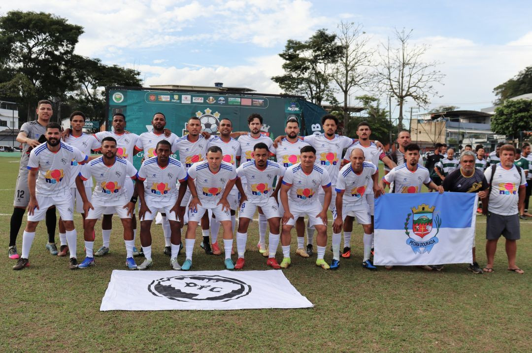 Foto oficial da equipe do Douradense posada no gramado durante o dia. Os jogadores vestem uniforme branco com detalhes em azul e vermelho e o patrocínio 