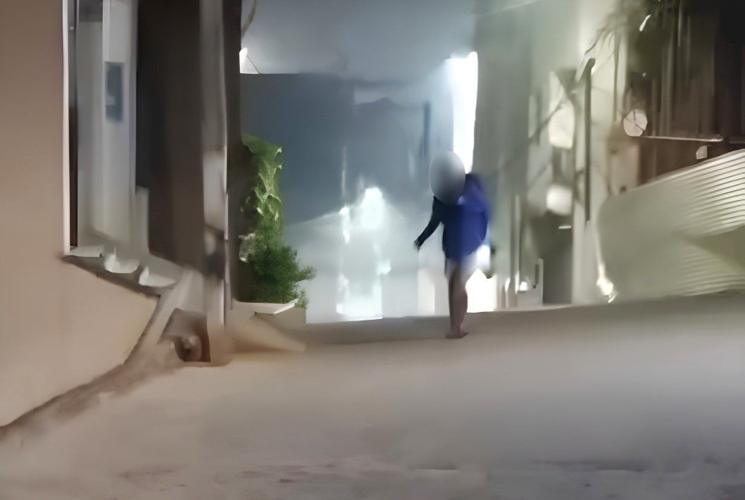 Uma imagem em plano aberto de um jovem sentado no chão, encostado em uma parede de concreto, em uma rua de Ibatiba. Ele veste um casaco azul marinho e calça jeans. Ele tem a cabeça baixa e as mãos apoiadas nos joelhos. A imagem está desfocada, mas é possível notar que ele parece estar em estado de desamparo. No fundo, há mais prédios e uma rua estreita. A imagem transmite uma sensação de isolamento e vulnerabilidade. A legenda da foto é: 