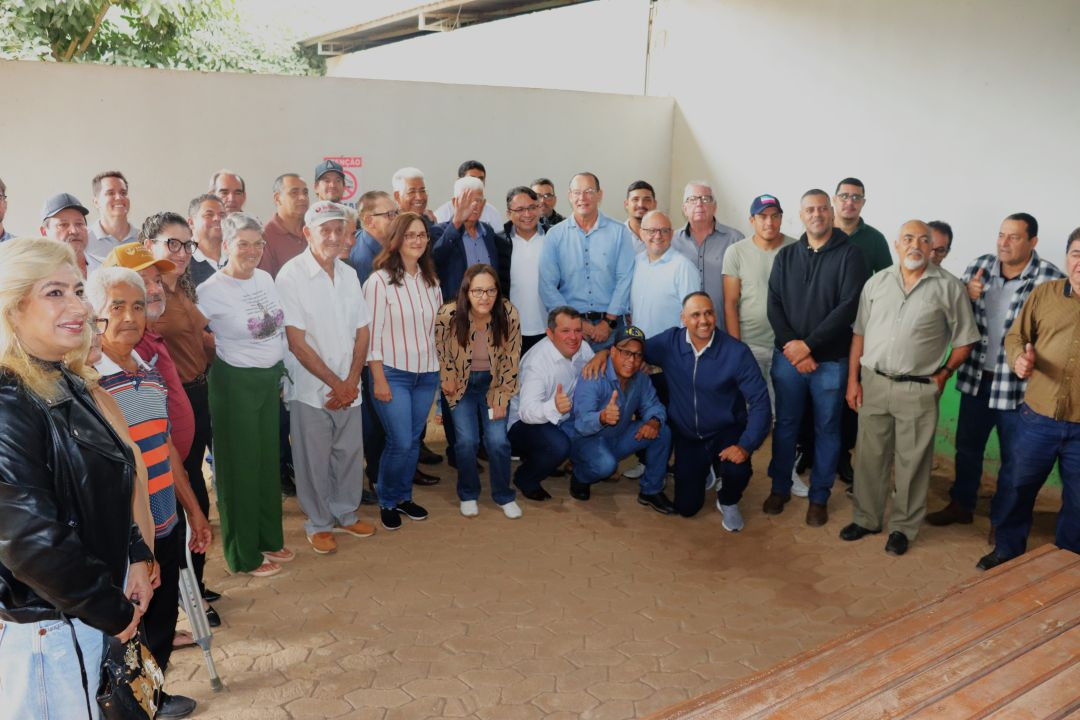 Foto oficial em grupo reunindo dezenas de moradores, produtores rurais e autoridades políticas locais. Eles estão sorrindo e posando juntos para a fotografia no interior do galpão de piso intertravado. Alguns homens na linha de frente aparecem agachados e fazendo sinal de positivo com o polegar.