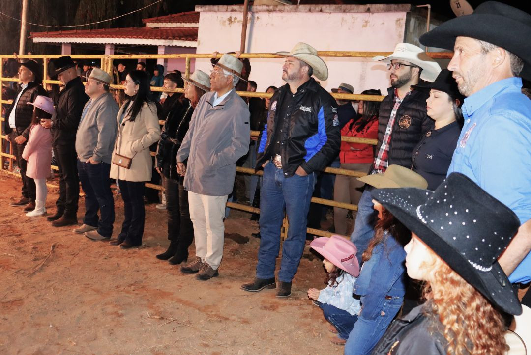 Imagem de perfil de um grupo de autoridades municipais e lideranças da região assistindo à 5ª Festa da Associação Carangolas. Eles estão em pé, próximos a uma cerca na arena de rodeio, com chapéus de cowboy e roupas formais. O prefeito de Ibatiba, Luiz Carlos Pancoti, e o presidente da Câmara Municipal, Marcus Rodrigo Amorim Florindo, estão visíveis entre eles.