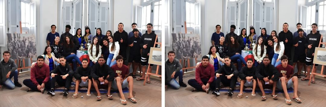 Foto coletiva com cerca de vinte pessoas, a maioria jovens e adolescentes, reunidos no interior do Solar Miguel Simão. Ao fundo, no centro, destaca-se a jovem coroada com trajes libaneses. Parte do grupo está em pé e a outra parte está sentada no chão de madeira. À esquerda, permanece o cavalete com a foto de família antiga e, à direita, outro cavalete exibe uma imagem histórica do prédio do solar.