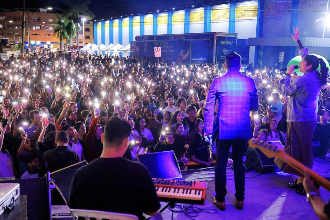 Vista do público reunido em frente ao palco durante show noturno na Praça do Fórum, em Iúna, com luzes de celulares acesas.