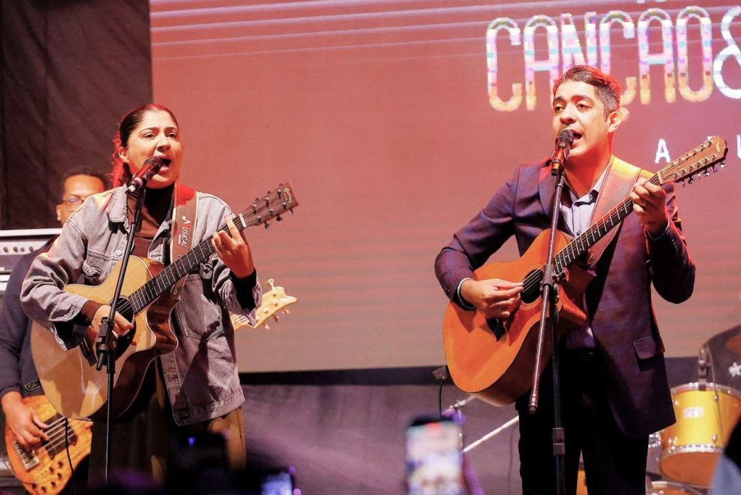 A dupla Canção e Louvor, formada pelos irmãos Cláudia e Cláudio, tocando violão e cantando no microfone.