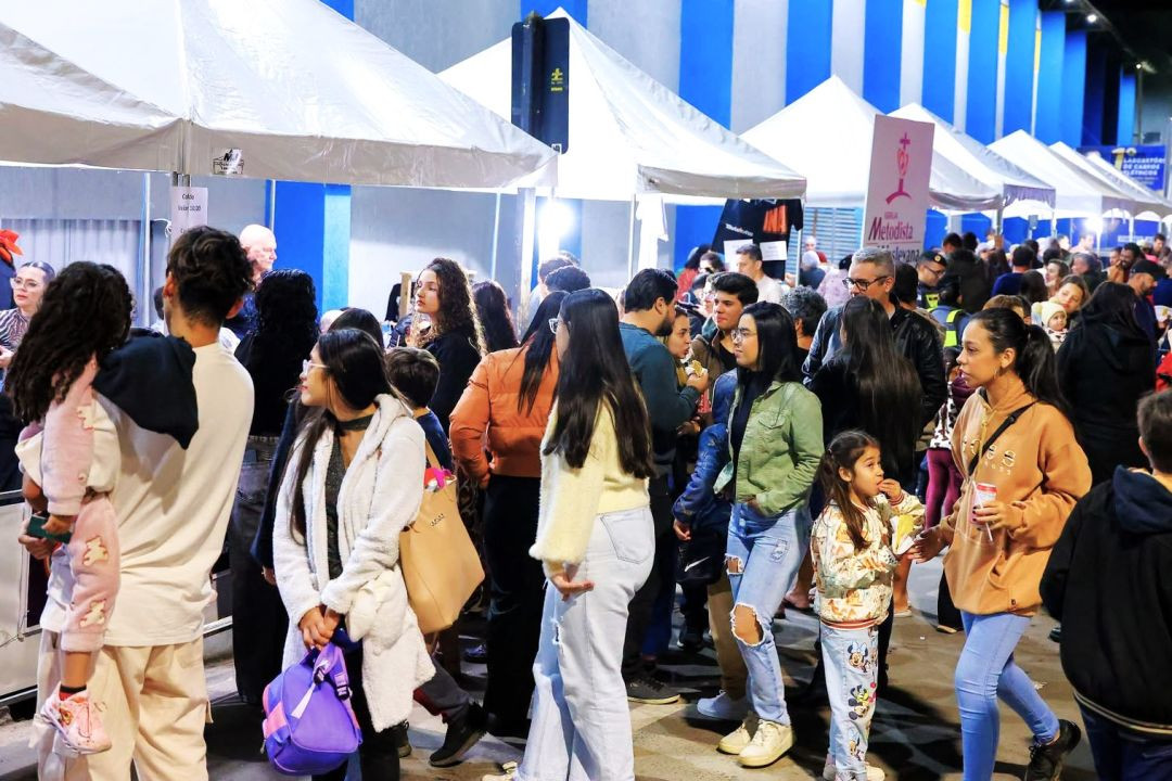 Pessoas de várias idades caminhando entre as tendas da Ação Global e de serviços montadas no local do evento.