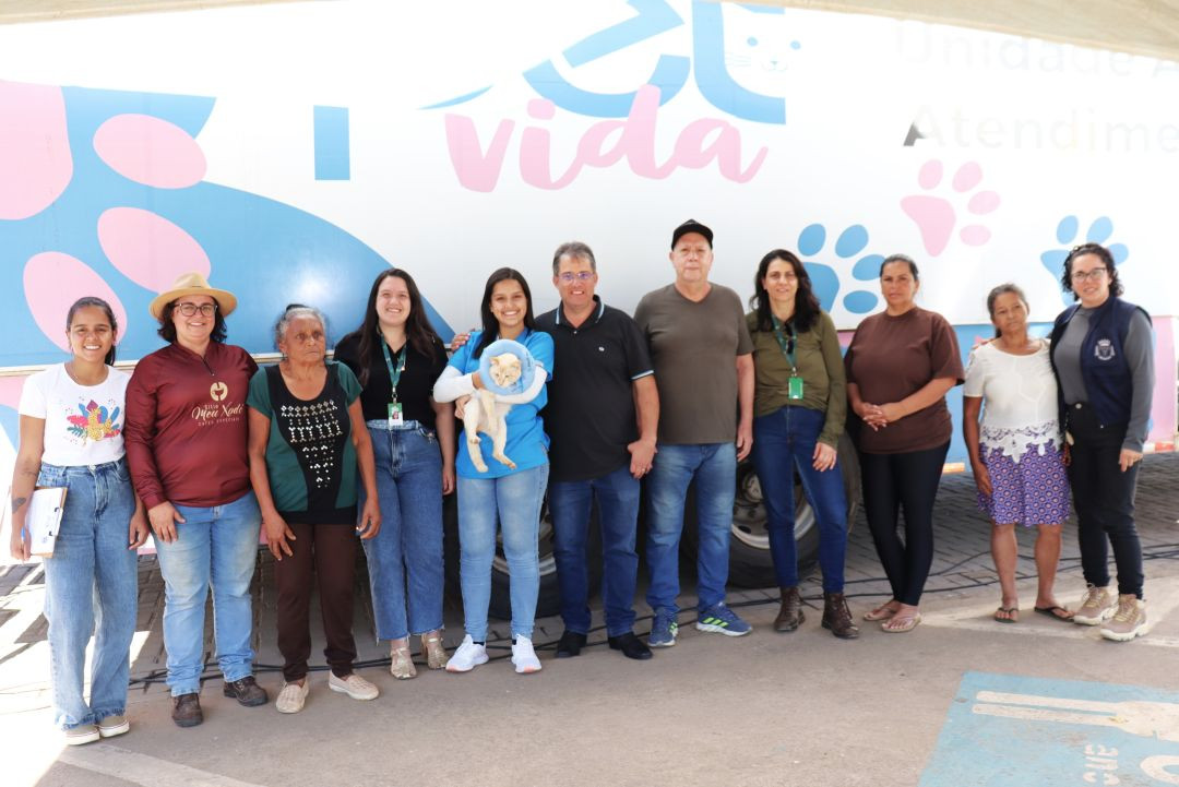 Grupo de dez pessoas, entre gestores públicos, voluntários e profissionais de saúde veterinária, posicionado em linha em frente ao veículo da unidade móvel do Programa Pet Vida. No centro, uma veterinária segura um gato de colar protetor azul.