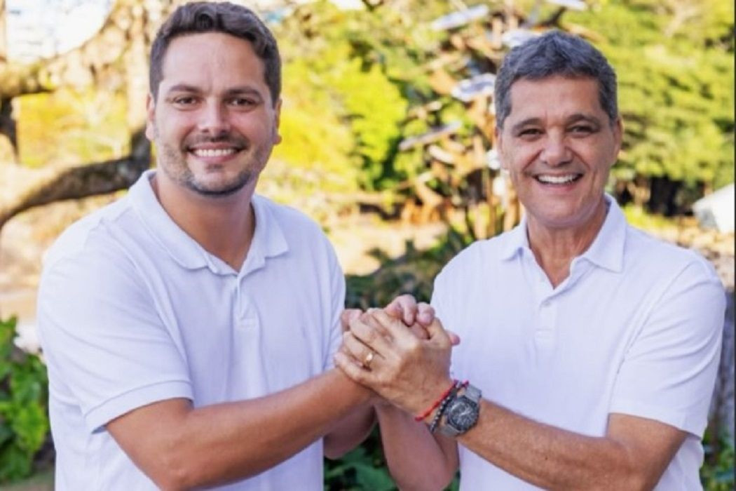 Ricardo Ferraço e Camillo Neves aparecem sorrindo, usando camisas brancas, enquanto se cumprimentam com um aperto de mãos em um ambiente ao ar livre.