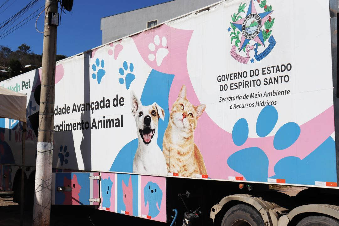 Carreta do programa Pet Vida estacionada, com identidade visual em branco, azul e rosa, ilustrações de um cão e um gato e o brasão do Governo do Estado do Espírito Santo na lateral. A unidade móvel é utilizada para oferecer serviços veterinários gratuitos, como castração e vacinação de cães e gatos.