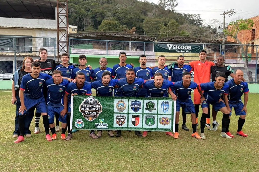 Fotografia de time de futebol com uniforme azul posando no gramado. Os jogadores da frente seguram um banner verde com a inscrição 