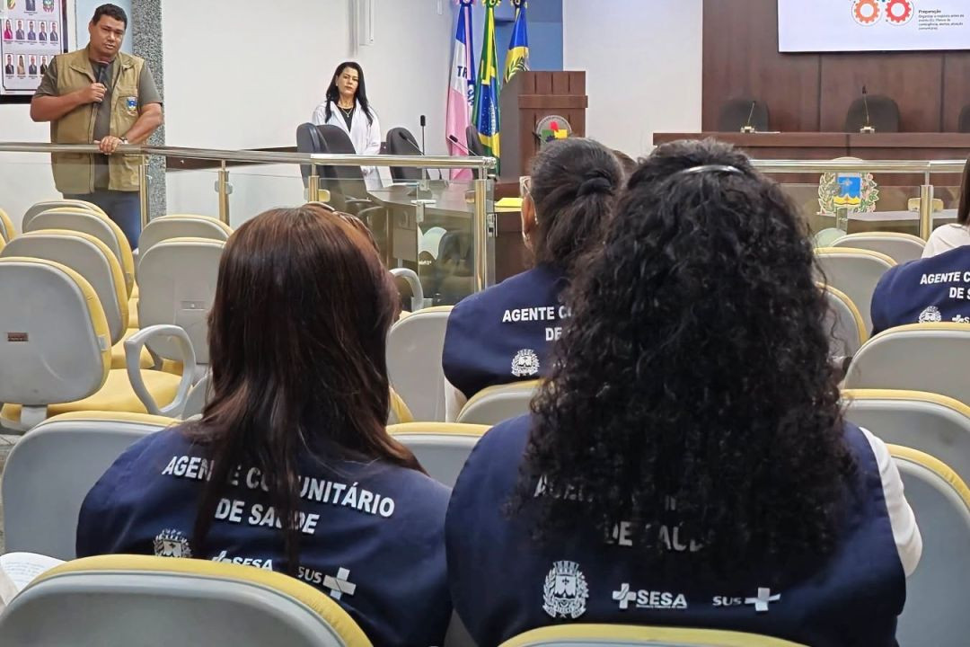 Fotografia em auditório mostrando profissionais da saúde de costas vestindo coletes azuis com as inscrições 