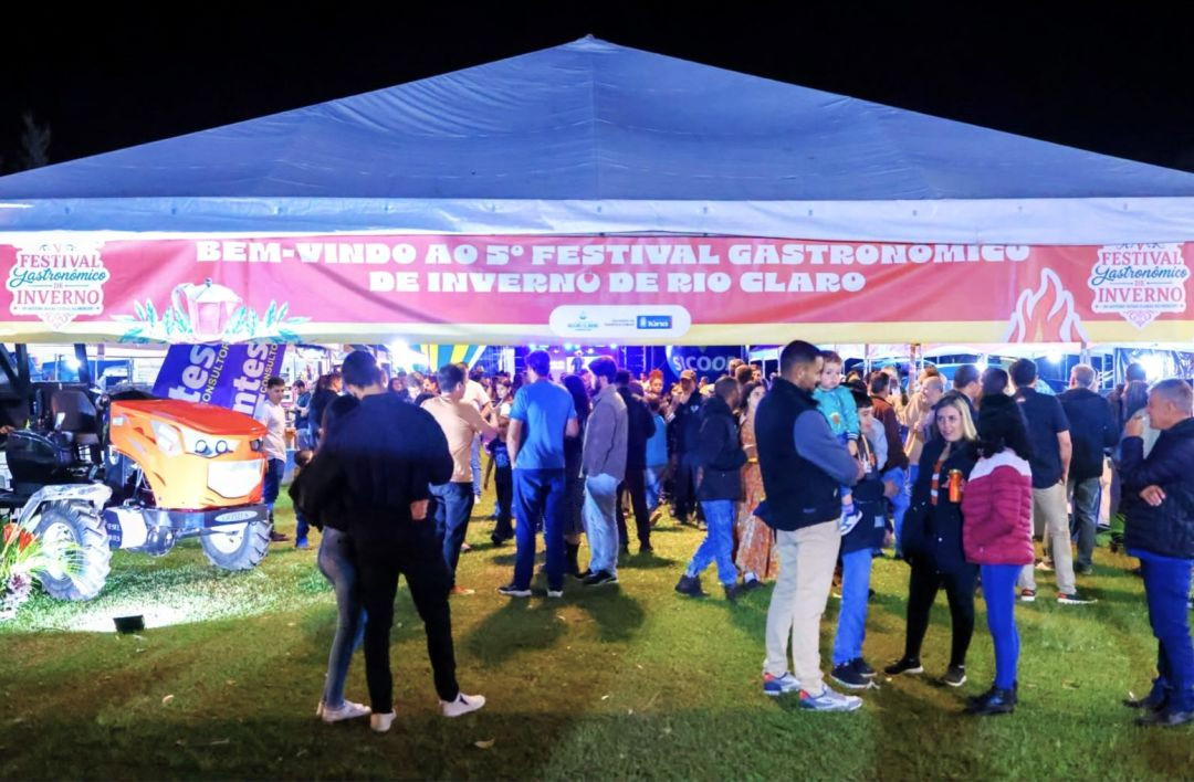 Entrada da tenda principal do festival com faixa indicativa contendo os dizeres 'Bem-vindo ao 5º Festival Gastronômico de Inverno de Rio Claro' e trator exposto na lateral esquerda.